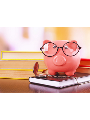 pink piggy bank wearing glasses sits on budget planning book in front of a stack of books