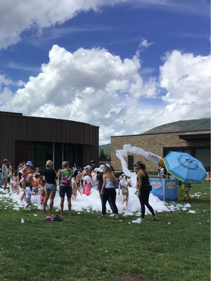 kids and parents play in giant foam bubbles on the library lawn.